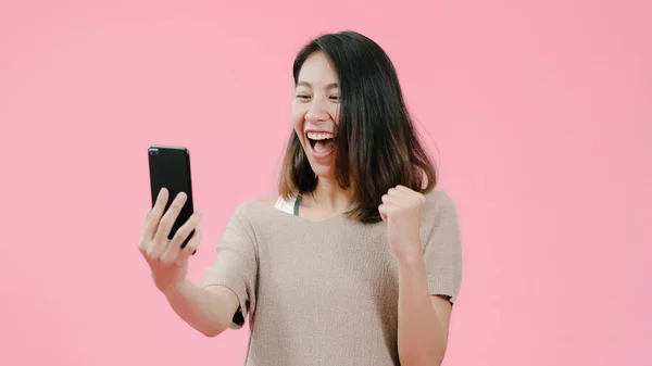 Ung asiatisk kvinne som bruker smarttelefon for å sjekke sosiale medier, smiler glad i løse klær med rosa bakgrunn. Lykkelig smilende, herlig glad kvinne fryder seg over suksess . – stockfoto