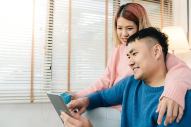 Çekici Asya tatlı çift kanepede yatan tablet kullanma ne zaman onların evde oturma odasında rahatlayın. Koca ve karısı kullanarak dinlenmek ve romantik zaman ev concept.