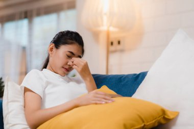 Genç Asyalı genç kadın oturma odasında kanepede yatarken cep telefonu oynadıktan sonra gözlerini ovuşturarak acı hissediyorum. Evde yaşam tarzı kadın ağrı kavramı.