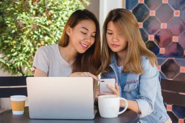 Asyalı Genç kadınlar kullanarak ve smartphone bakarak ve içme kahve kafede otururken dizüstü bilgisayar üzerinde çalışan. Yaşam tarzı kadın iletişim ve kahve dükkanı kavramı içinde çalışma.