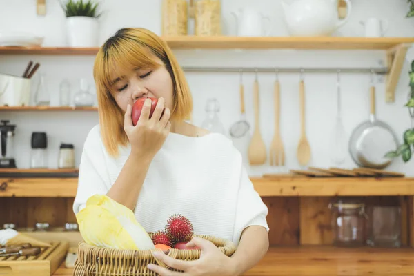 Asiatisk vakker kvinne spiser rødt eple på kjøkkenet hjemme hos seg. Lykkelig, søt asiatisk kvinne spiser frisk frukt for en sunn kropp. livsstil asiatisk kvinne som hjemmebegrep . – stockfoto