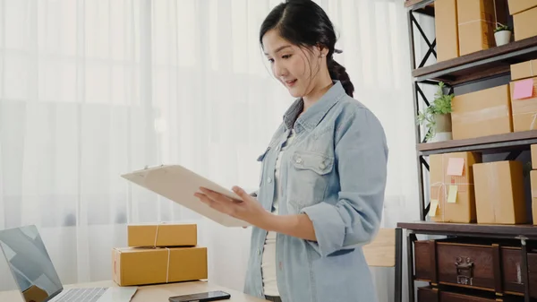 Gyönyörű ázsiai intelligens fiatal vállalkozó nő cégtulajdonos a KKV-k ellenőrzése termék raktáron, és írni a vágólapra otthoni munkavégzés. Kisvállalkozás tulajdonosa, otthoni iroda koncepció:. — Stock Fotó