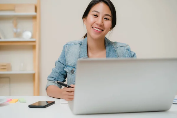Kaunis nuori hymyilevä aasialainen nainen työskentelee kannettavan tietokoneen työpöydällä olohuoneessa kotona. Aasia liiketoiminnan nainen kirjoittaa kannettavan asiakirjan rahoituksen ja laskin kotona toimistossa. Nauti aikaa kotona käsite . — kuvapankkivalokuva