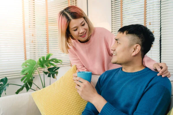 Atractiva pareja asiática dulce disfrutar de momento de amor beber taza de café caliente o té en sus manos en el sofá en la sala de estar en casa. Marido y su esposa relajándose en el concepto de casa . —  Fotos de Stock