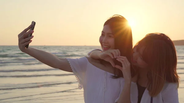 Unga asiatiska lesbisk par med smartphone tar Selfie nära stranden. Vackra kvinnor hbt-par Happy Relax Njut av kärleks ögonblick när solnedgången på kvällen. Livsstil lesbisk par resa på Beach Concept — Stockfoto