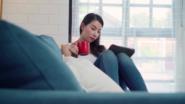 거실에서 편안하게 소파에 커피나 태블릿을 아름다운 미소짓는 아시아 에서의 — 비디오