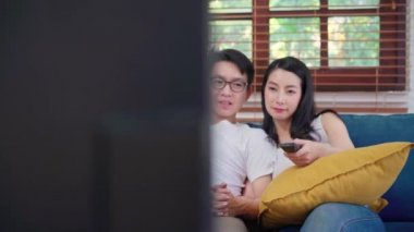 Evdeki oturma odasında televizyon izleyen Asyalı çift, evde dinlenirken kanepede uzanan tatlı çift aşk anının tadını çıkarıyor. Yaşam tarzı çifti ev kavramında rahatlar..