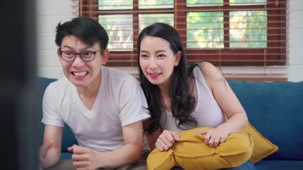 亚洲夫妇在家里的电视客厅前欢呼足球比赛 甜蜜的夫妇在家里放松的时候躺在沙发上享受着有趣的时刻 生活方式夫妻在家里放松一下 — 图库视频影像