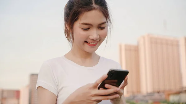 Asiatisk turistblogger bruker touchscreen-teknologi på smarttelefon mens hun går på gata i sentrum av byen om kvelden . – stockfoto