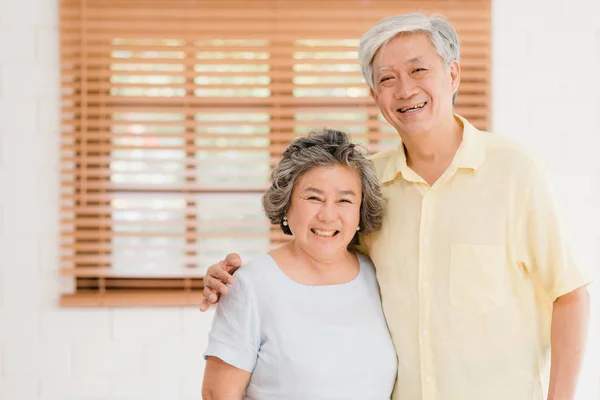 Asiatisches älteres Paar, das glücklich lächelnd in die Kamera blickt, während es sich zu Hause im Wohnzimmer entspannt. Genießen Sie die Zeit Lebensstil Seniorenfamilie zu Hause Konzept. Porträt mit Blick auf die Kamera. — Stockfoto