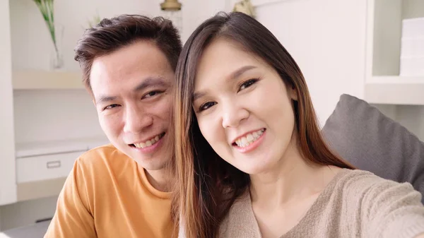 Asian couple using smartphone VIDEO Call with friend in living room at home, sweet couple enjoy love moment while lying on the sofa when relaxed at home. Lifestyle couple relax at home concept.