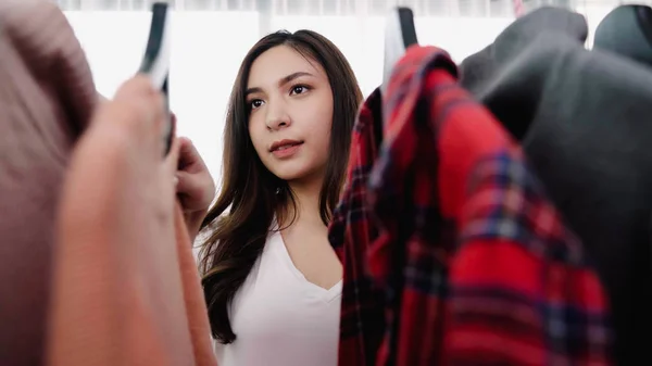 Hem garderob eller klädbutik omklädningsrum. Asiatisk ung kvinna att välja hennes mode outfit kläder i garderoben hemma eller store. Flicka tycker vad att bära tröja. — Stockfoto