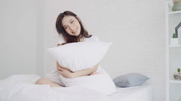 En lykkelig, vakker asiatisk kvinne våkner og smiler og strekker armene i sengen sin på soverommet. Ung asiatisk kvinne bruker avslapningstid hjemme. Livsstilsdame hjemme . – stockfoto