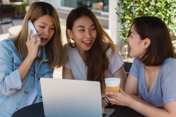 Asiático mujeres jóvenes que trabajan en el ordenador portátil usando y mirando teléfono inteligente y beber café mientras está sentado en la cafetería . — Foto de Stock