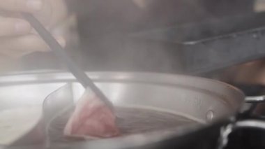 Japon restoranında sıcak tencere yiyen Asyalı kadın, yemek çubuklarıyla dilimlenmiş dana eti tutan genç kadın öğle yemeğinde şabu yiyor. Yaşam tarzı kadınlar yemek kavramı yiyor. Yavaş çekim çekimi.