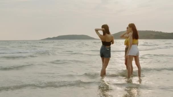 携帯電話の写真撮影やビーチで遊ぶアジアの女性のグループは 美しい女性は夕方の日没時に海の近くのビーチでリラックスします 夏のコンセプトでビーチで女性旅行 — ストック動画