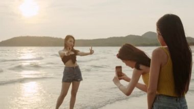 Cep telefonu fotoğrafçılığı kullanan ve sahilde oynayan Asyalı kadın grubu, Güzel kadın akşam gün batımında denize yakın plajda dinlenmek. Yaz konseptinde sahilde kadın seyahati.