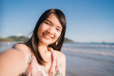 Sahilde turist Asyalı kadın selfie, genç güzel kadın mutlu cep telefonu kullanarak gülümseyerek akşam gün batımında deniz kenarında sahilde selfie çekerek. Yaşam tarzı kadın plaj konsepti seyahat.