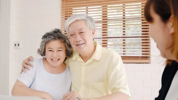 Asia agente femenino inteligente ofrece seguro de salud para parejas de ancianos por documento, tableta y computadora portátil. Envejecido asiático pareja consultando con el agente de seguros mientras se sienta junto con en casa . — Foto de Stock