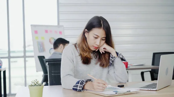 Profesjonell asiatisk forretningskvinne som jobber på kontoret via en bærbar datamaskin. Ung asiatisk kvinnelig leder som bruker bærbar dataenhet mens han sitter på moderne arbeidsplass . – stockfoto
