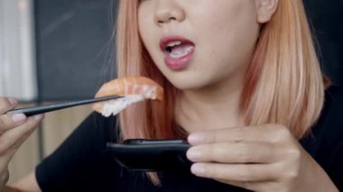 Japon restoranında suşi yiyen Asyalı kadın, yaz aylarında öğle yemeğinde yemek yiyen genç kadın. Yaşam tarzı kadınlar geleneksel gıda kavramı yiyor. Yavaş çekim çekimi.