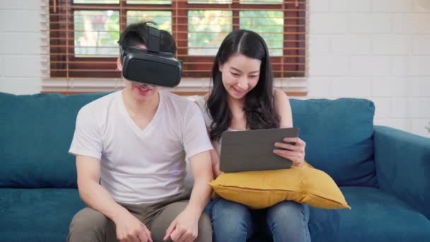 亚洲夫妇使用平板电脑和虚拟现实模拟器在客厅里玩游戏 情侣们开心地坐在家里的桌子上 生活方式家庭放松在家里的概念 — 图库视频影像