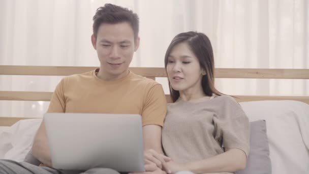 寝室でリラックスしているときにベッドに横たわっている間にラップトップを使用するアジアのカップル 自宅でコンピュータでソーシャルメディアを再生するカップル 自宅のコンセプトでリラックスタイムを使用してカップル — ストック動画