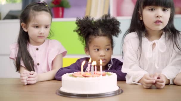 スローモーション 子供たちは教室で誕生日のパーティーを祝う 多民族の若い女の子は幸せに学校でバースデーケーキにキャンドルを吹き消す願いを作ります 子供たちは学校のコンセプトで誕生日を祝う — ストック動画