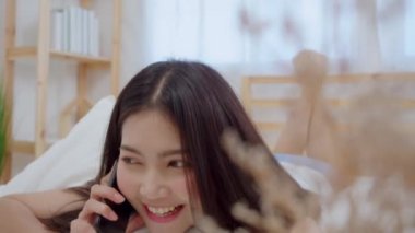 Genç Asyalı kadın uyan sabah, sonra yatakta yatıyordu süre Smartphone kullanarak gülümseyen güzel çekici Japon kız evde yatak odasında rahatlayın. Ev concept zaman yaşam tarzı kadınlar enjoying.
