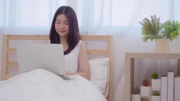 年轻的商业自由职业亚洲妇女工作在笔记本电脑检查社交媒体 而躺在床上 当放松在卧室在家里 生活方式 女性在房子的概念 — 图库视频影像
