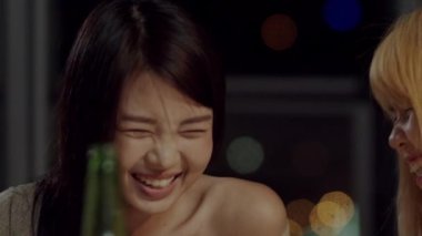 Bira kızartma ve evde kutlayan içecek şişeleri ile gülerek ve genç Asyalı arkadaşlar grubu. Mutlu genç arkadaşlar yaz gecesi parti kutlamamüzik dinlerken. Yavaş çekim çekimi.