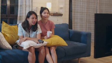 Lezbiyen lgbt kadın çift evde televizyon izlerken, Asyalı kadın sevgilisi mutlu komik an gece konsepti oturma odasında kanepede birlikte drama eğlence görünümlü duygu.