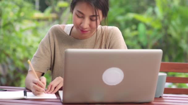 自宅で働くフリーランスのアジア人女性 午前中に庭のテーブルの上に座ってノートパソコンで働くビジネス女性 家庭のコンセプトで働くライフスタイルの女性 — ストック動画