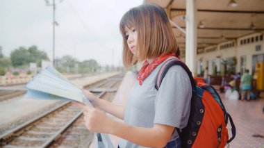 Gezgin Asyalı kadın yön ve tatil gezi ve bekleyen tren tren istasyonunda harcama ise konumu harita üzerinde seyir, genç kadın turist backpacker yolculuk keyfini çıkarın. Yaşam tarzı kadın seyahat kavramı