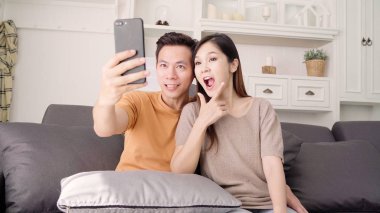 Asya çift evde oturma odasında selfie için Smartphone kullanarak, tatlı çift evde rahat zaman kanepede yatarken aşk anın tadını çıkarın. Yaşam tarzı çift evde kavramı relax.
