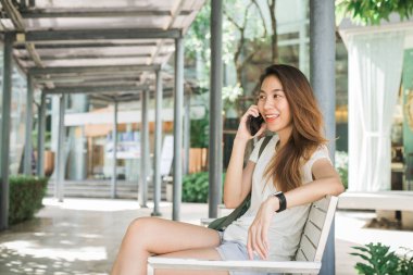 Güzel Asyalı genç kadın konuşmak için akıllı telefon kullanarak, okuma ve yaz ve güneşli bir gün şehir şehir bankta oturan mesajlaşma. Yaşam tarzı kadınlar seyahat ve şehir kavramı dinlenmek.