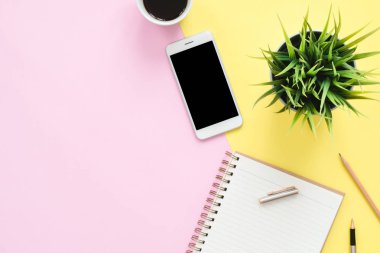 Ofis Masası adlı kullanıcının alanı - düz çalışma beyaz boş defter sayfası, kahve fincanı ve sahte telefon pastel arka plan üzerinde bir çalışma alanının en iyi görünümü yatırın. Pastel pembe sarı renk arka plan boşluk kavramı.
