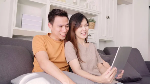 Pareja asiática usando tableta VIDEO Llamar con un amigo en la sala de estar en casa, dulce pareja disfrutar del momento de amor mientras se acuesta en el sofá cuando se relaja en casa. Estilo de vida pareja relajarse en el hogar concepto . — Foto de Stock