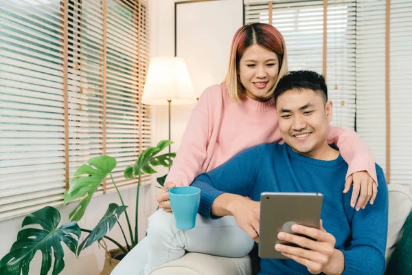 Atractiva pareja asiática dulce usando tableta mientras está acostado en el sofá cuando relajarse en su sala de estar en casa. Esposo y su esposa usando relajarse y tiempo romántico en el concepto de casa . — Foto de Stock