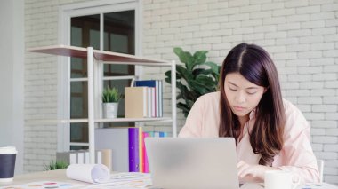 Asyalı kadın çalışma dizüstü evde oturma odasında masa üzerinde gülümseyen güzel genç. Asya iş kadını defter belge finans ve hesap makinesi ev ofis yazma. Ev concept anda zevk.