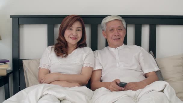 亚洲老年夫妇在家卧室看电视 亚洲夫妇一边享受爱情时刻 一边躺在床上放松地在家 享受时间生活方式老年家庭观念 慢动作拍摄 — 图库视频影像