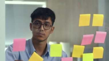 Asyalı yaratıcı adam cam tahta üzerinde yapışkan bir not sopa. Genç profesyonel iş erkek yazma bilgi, strateji, kağıt üzerinde hatırlatma, iş durumu, Loft ofis kavramı başlangıç.