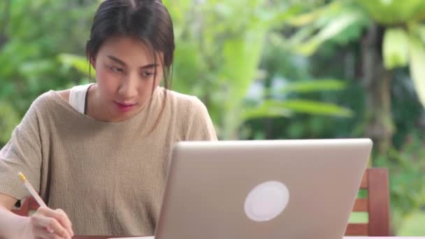 自宅で働くフリーランスのアジア人女性 午前中に庭のテーブルの上に座ってノートパソコンで働くビジネス女性 家庭のコンセプトで働くライフスタイルの女性 — ストック動画