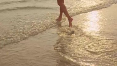 Kum sahilinde koşan Asyalı bir kadın. Bikini li genç mutlu kadın, tatil, tatil, yaz gezisi konsepti, tatil, tatil, yaz gezisi konsepti, gün batımı sırasında tropikal deniz kenarında eğlenceli bir şekilde koşar. Yavaş çekim çekimi.
