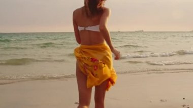 Kum sahilinde koşan Asyalı bir kadın. Bikini li genç mutlu kadın, tatil, tatil, yaz gezisi konsepti, tatil, tatil, yaz gezisi konsepti, gün batımı sırasında tropikal deniz kenarında eğlenceli bir şekilde koşar. Yavaş çekim çekimi.