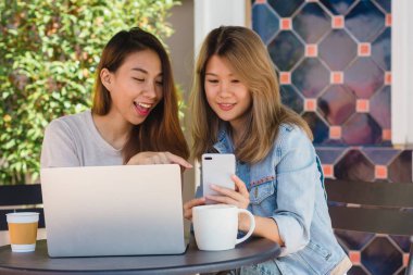 Asyalı Genç kadınlar kullanarak ve smartphone bakarak ve içme kahve kafede otururken dizüstü bilgisayar üzerinde çalışan. Yaşam tarzı kadın iletişim ve kahve dükkanı kavramı içinde çalışma.