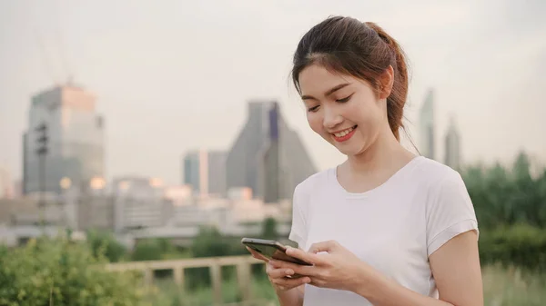 Iloinen aasialainen turisti bloggaaja nainen käyttää kosketusnäyttö teknologiaa älypuhelimella kävellessään kadulla keskustan kaupungin illalla. Elämäntapa reppu turisti matka loma käsite . — kuvapankkivalokuva