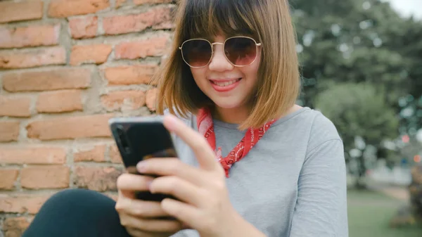 Reisende asiatisk kvinne som bruker smarttelefon for å sjekke sosiale medier mens hun slapper av etter å ha vært på ferie på Ayutthaya, Thailand, nyter sin reise på et fantastisk landemerke i tradisjonell by . – stockfoto