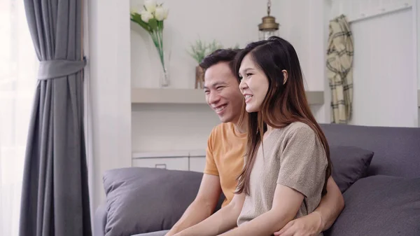 Asian couple watching TV and drinking warm cup of coffee in living room at home, sweet couple enjoy love moment while lying on the sofa when relax at home. Lifestyle couple relax at home concept.