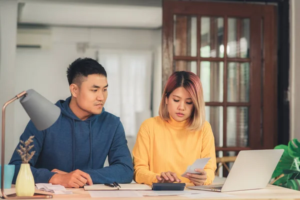Nuori aasialainen pari, joka hallinnoi taloutta, tarkistaa pankkitilinsä kannettavan tietokoneen ja laskimen avulla nykyaikaisessa kodissa. Nainen ja mies tekevät paperityötä yhdessä, maksaa veroja verkossa kannettavan tietokoneen . — kuvapankkivalokuva